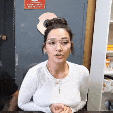 a woman wearing glasses is sitting in front of a sign that says " lubricates perfectly "