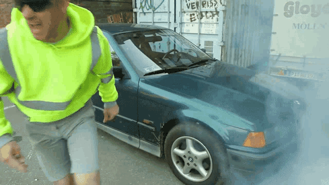 a man standing next to a car with smoke coming out of it and a sign that says verriss bitch