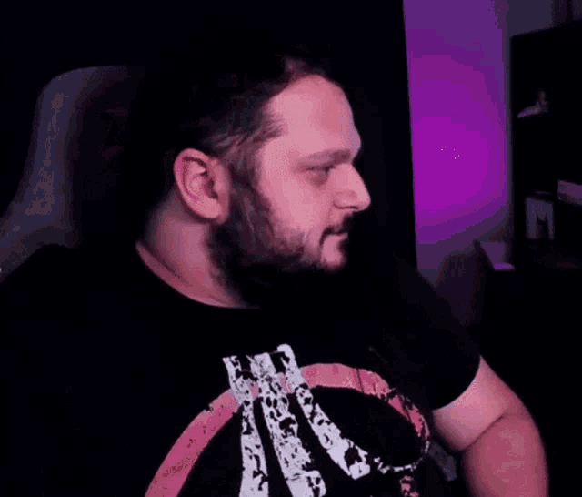 a man with a beard wearing a black shirt with the letter k on it