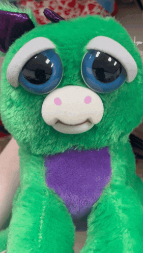 a green stuffed animal with blue eyes and a purple heart on its chest