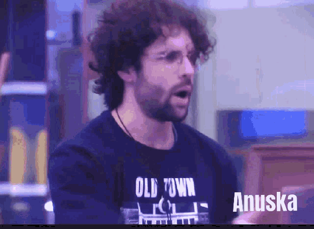 a man with curly hair and glasses wearing an old town shirt