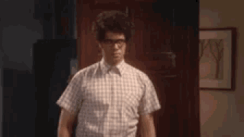 a man wearing glasses and a plaid shirt is standing in front of a door in a room .