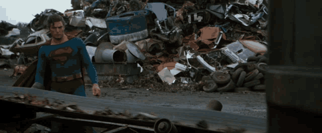a man in a superman costume is standing in front of a pile of scrap metal
