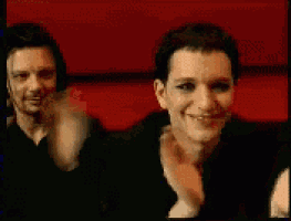 a man in a black suit is smiling while another man covers his mouth