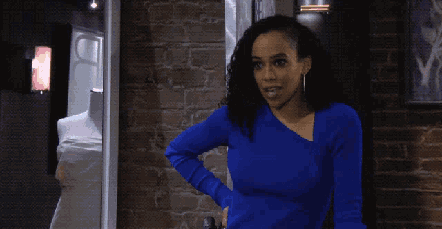 a woman wearing a blue sweater stands in front of a brick wall