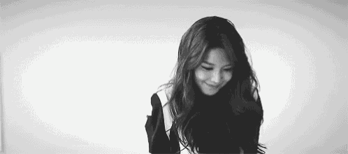 a black and white photo of a woman with long hair and a smile on her face .