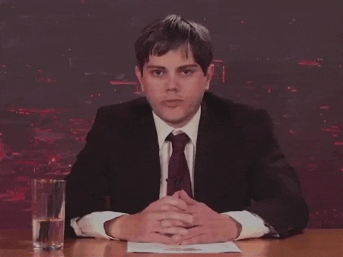 a man in a suit and tie sitting at a desk with his hands folded