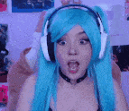 a woman with blue hair and headphones is covering her mouth .