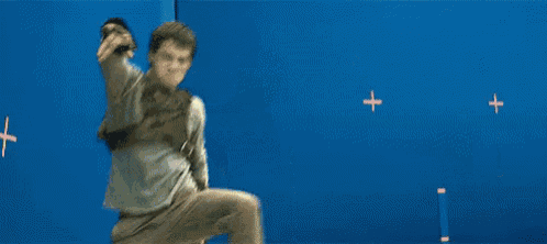a man is standing on one leg in front of a blue wall with a red cross on it .