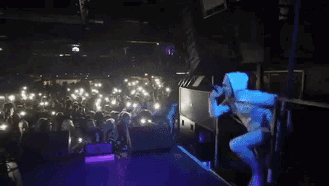 a man in a white hoodie stands on a stage with a crowd watching