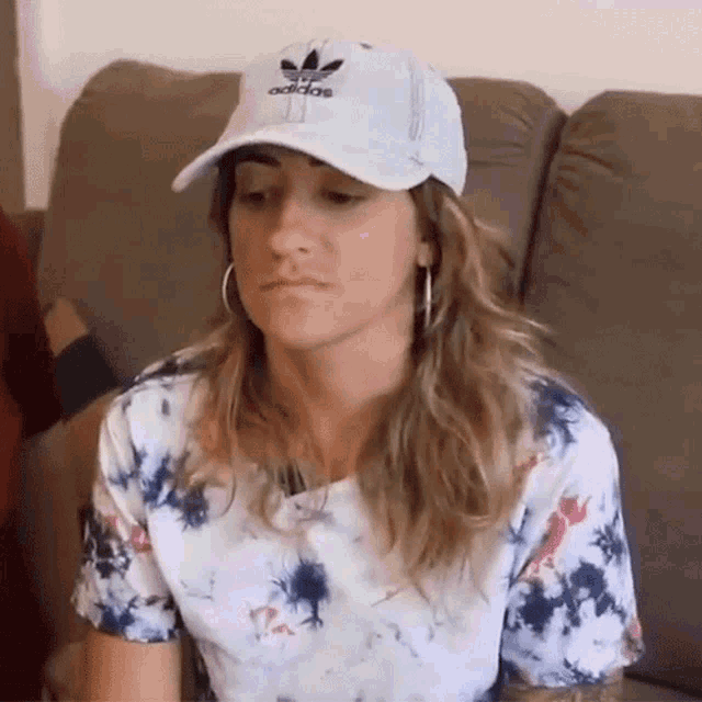a woman is sitting on a couch wearing a hat and a tie dye shirt .