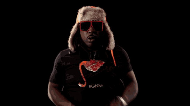 a man wearing a fur hat and sunglasses is standing with his arms crossed