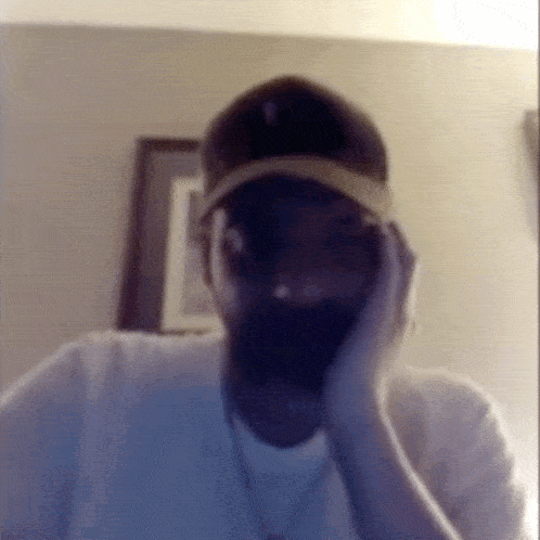 a man wearing a baseball cap covering his face with his hand