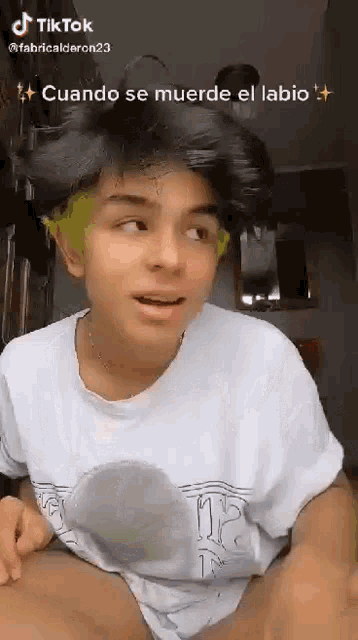 a young man with green hair is wearing a white t-shirt and making a funny face .