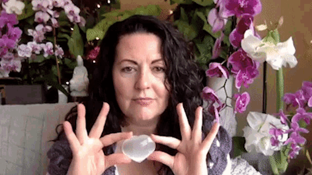a woman is holding a clear crystal in her hands in front of purple flowers .