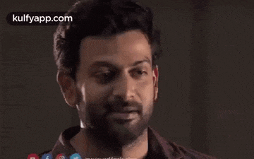 a man with a beard is smiling and looking at the camera while standing in a dark room .