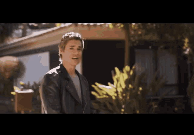 a man in a black leather jacket is standing in front of a house