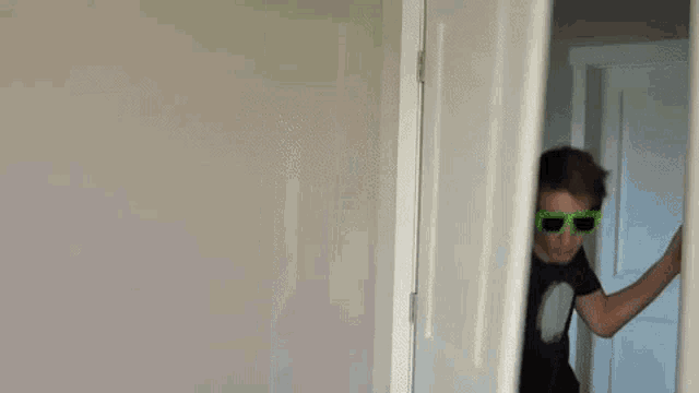 a young man wearing sunglasses and a black shirt is standing in a doorway .
