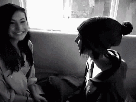 a man and a woman are sitting next to each other in front of a window . the woman is wearing a beanie .