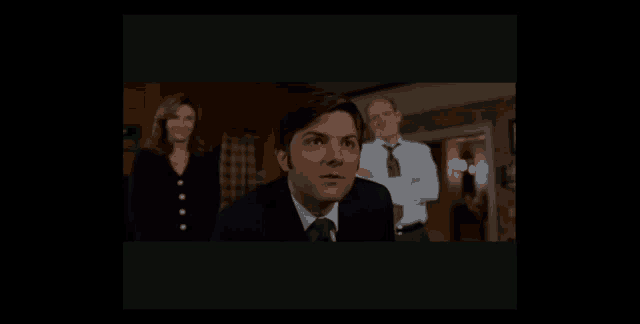 a man in a suit and tie stands in front of a woman and a man with his arms crossed