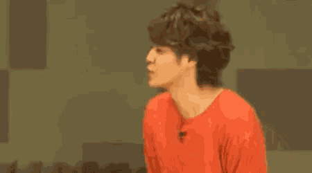 a man in a red shirt is standing in front of a green wall and making a funny face .