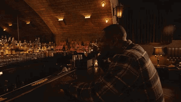 a man in a plaid shirt sits at a bar drinking