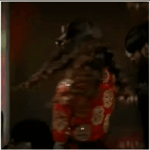 a woman in a red and gold dress is dancing in a dark room .