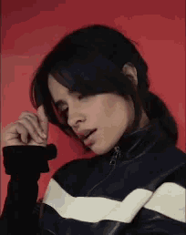a woman wearing a black and white striped jacket is standing in front of a red wall .