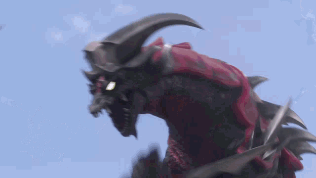 a red and black monster with horns and sharp teeth against a blue sky