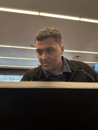 a man in a blue shirt and black jacket is looking at a computer screen
