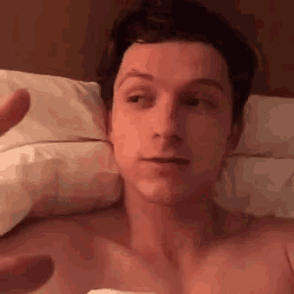 a shirtless man is laying in bed making a funny face and waving .