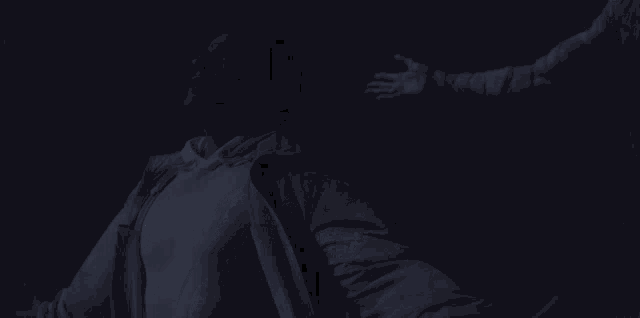 a man in a white shirt is standing in the dark with his arm outstretched