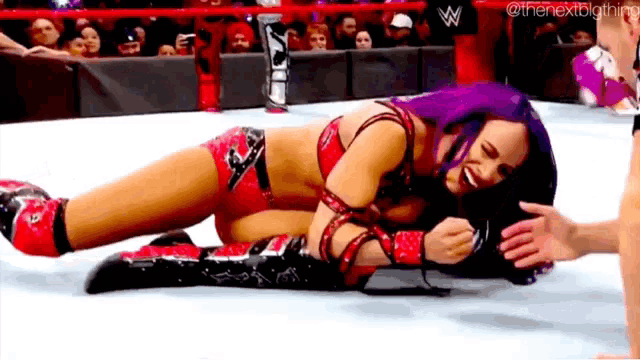 a female wrestler is laying on the ground in a wrestling ring while a man holds her hand .