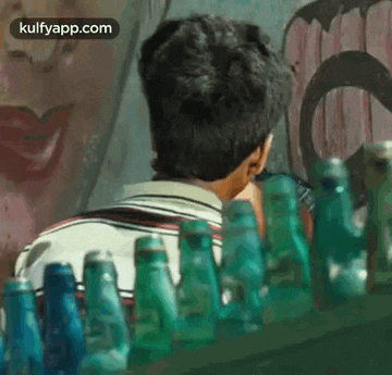 a man is standing in front of a row of empty green bottles .