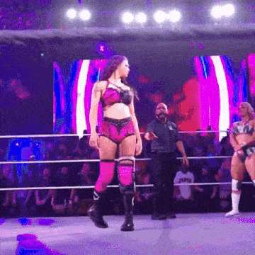 a female wrestler in a pink outfit is walking around the ring