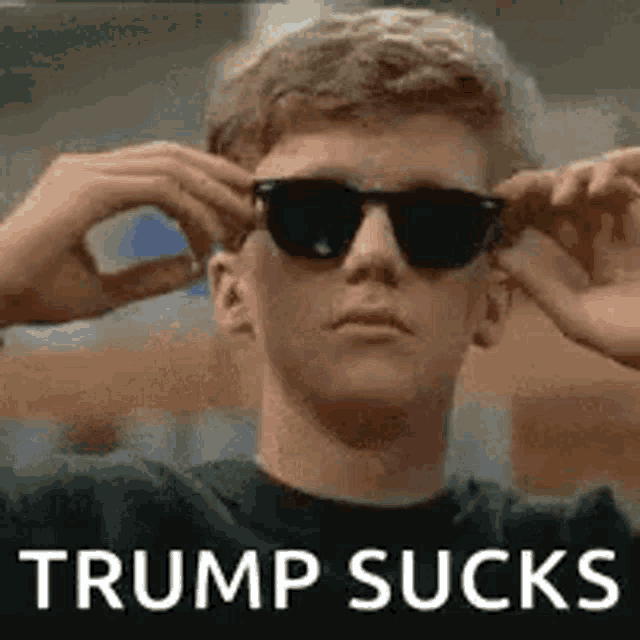 a man wearing sunglasses is making a funny face and says trump sucks .