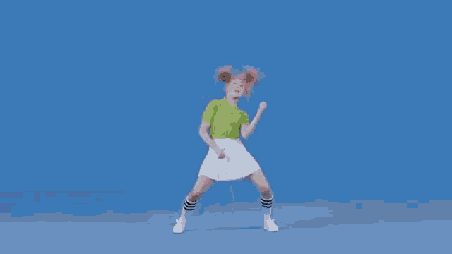 a woman in a green shirt and a white skirt is dancing on a blue background .
