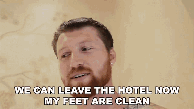 a shirtless man with a beard is smiling and says we can leave the hotel now my feet are clean