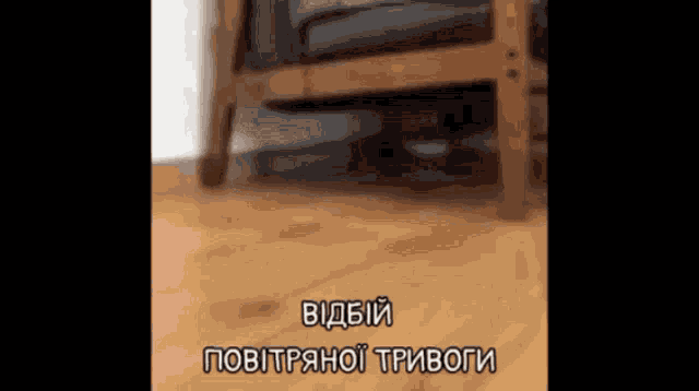 a blurred image of a chair and a wooden floor with a caption in a foreign language ..