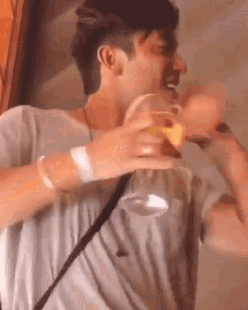a man in a gray shirt is holding a glass of beer and laughing .