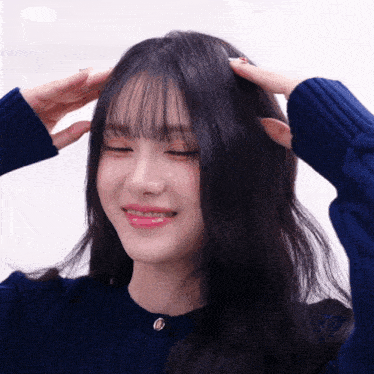 a woman wearing a blue sweater has her eyes closed and her hands on her head