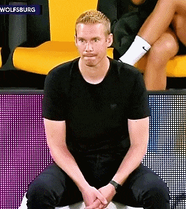a man in a black shirt is sitting in front of a sign that says " wolfsburg "