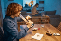 a man is smoking a bong while sitting at a table in a living room .