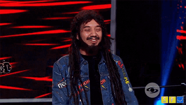 a man with long hair is giving a peace sign while standing on a stage