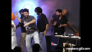 a group of men are dancing on a stage in front of a table with plates of food .