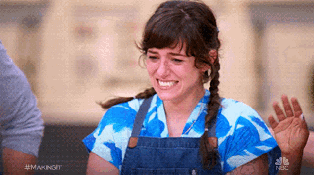 a woman in a blue shirt and overalls is smiling and waving while making a funny face ..