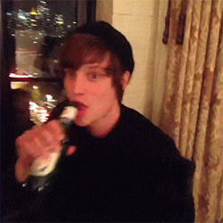 a young man is drinking from a bottle in a dark room