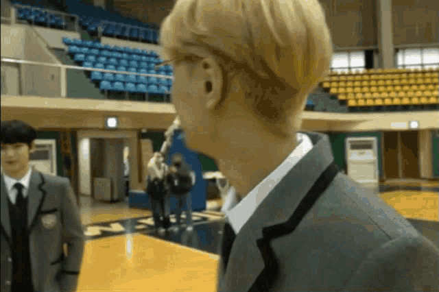 a man in a suit and tie stands on a basketball court in front of bleachers