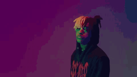 a man wearing a hoodie with dreadlocks is standing in front of a purple background .
