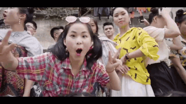 a girl wearing sunglasses and a plaid shirt is making a peace sign